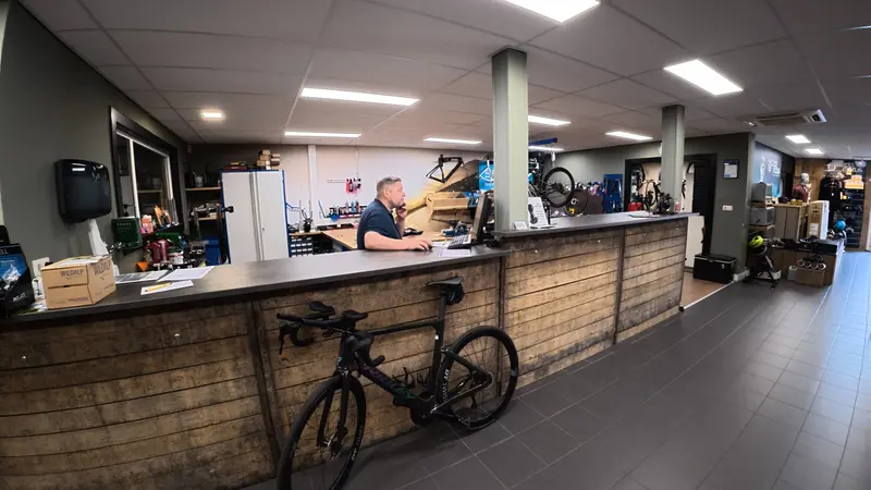 Remco achter de balie van Vision Sports met een racefiets ernaast