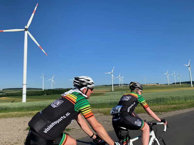 Wielrenners in Vision Sports-tenue langs een windmolenpark